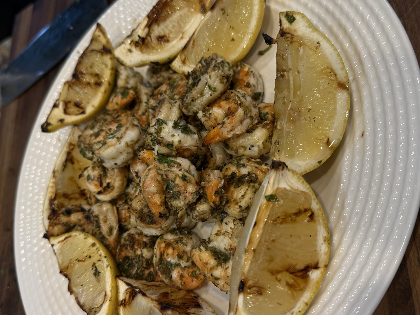 Grilled lemon garlic shrimp tossed with fresh herbs and charred lemon wedges on a white plate