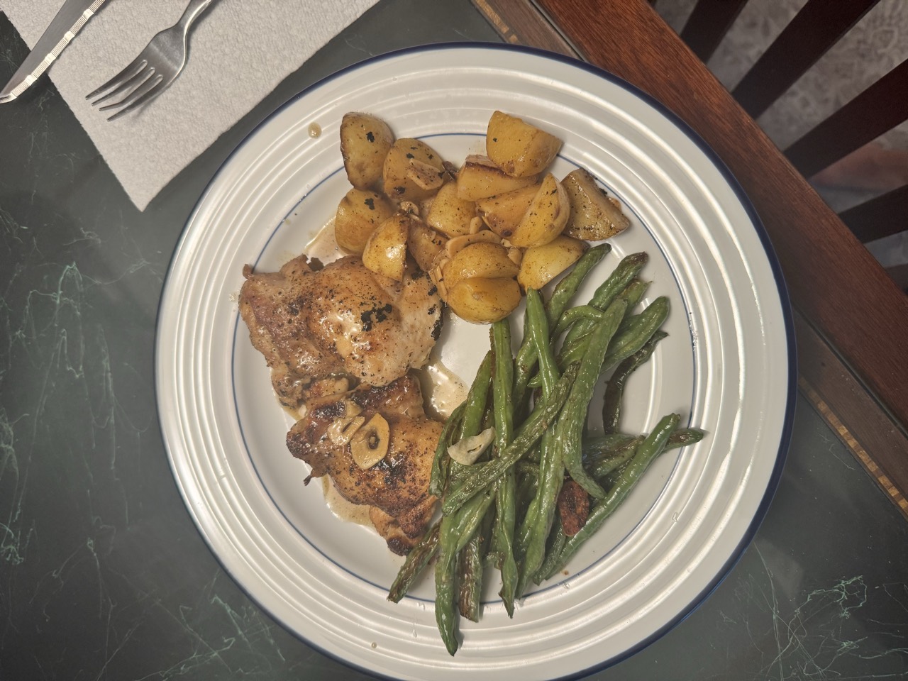 Crispy lemon chicken thighs with roasted lemon potatoes and blistered green beans on a white plate