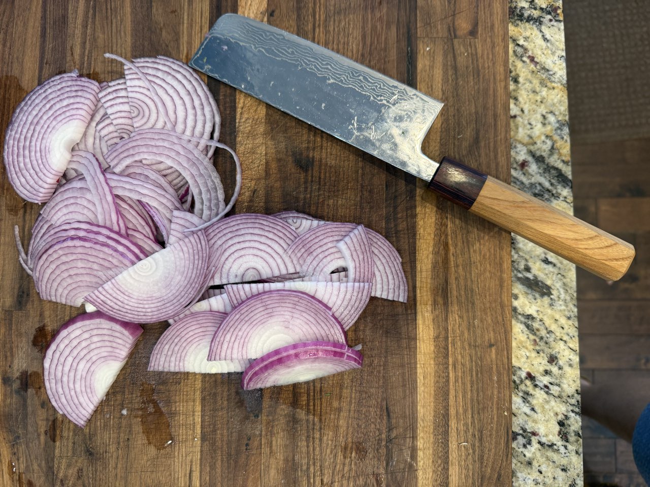 Thinly sliced purple onions on a cutting board, ready to caramelize