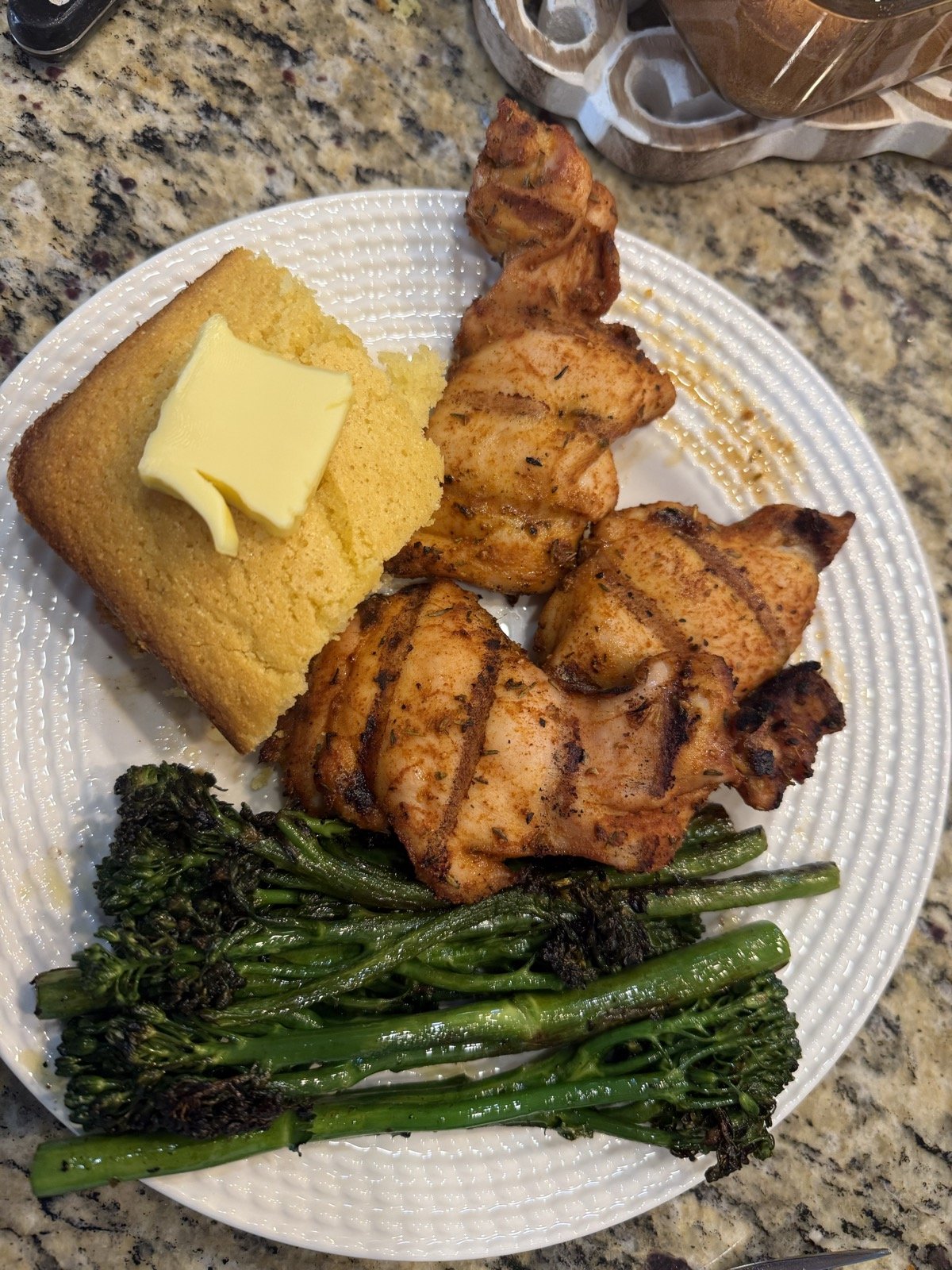 Grilled Cajun-spiced chicken thighs with a buttered square of cornbread and charred broccolini on a white plate