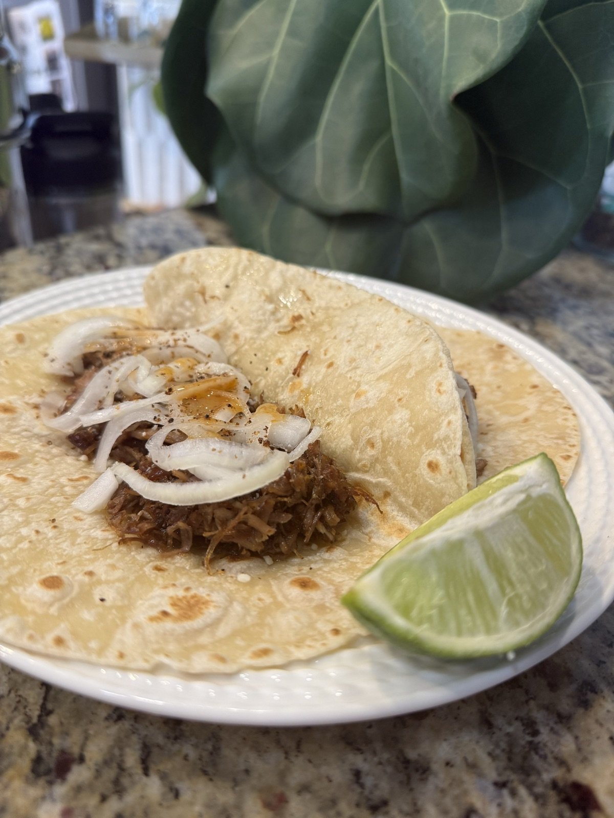 A warm tortilla filled with crispy carnitas, pickled red onions, and cilantro with a lime wedge