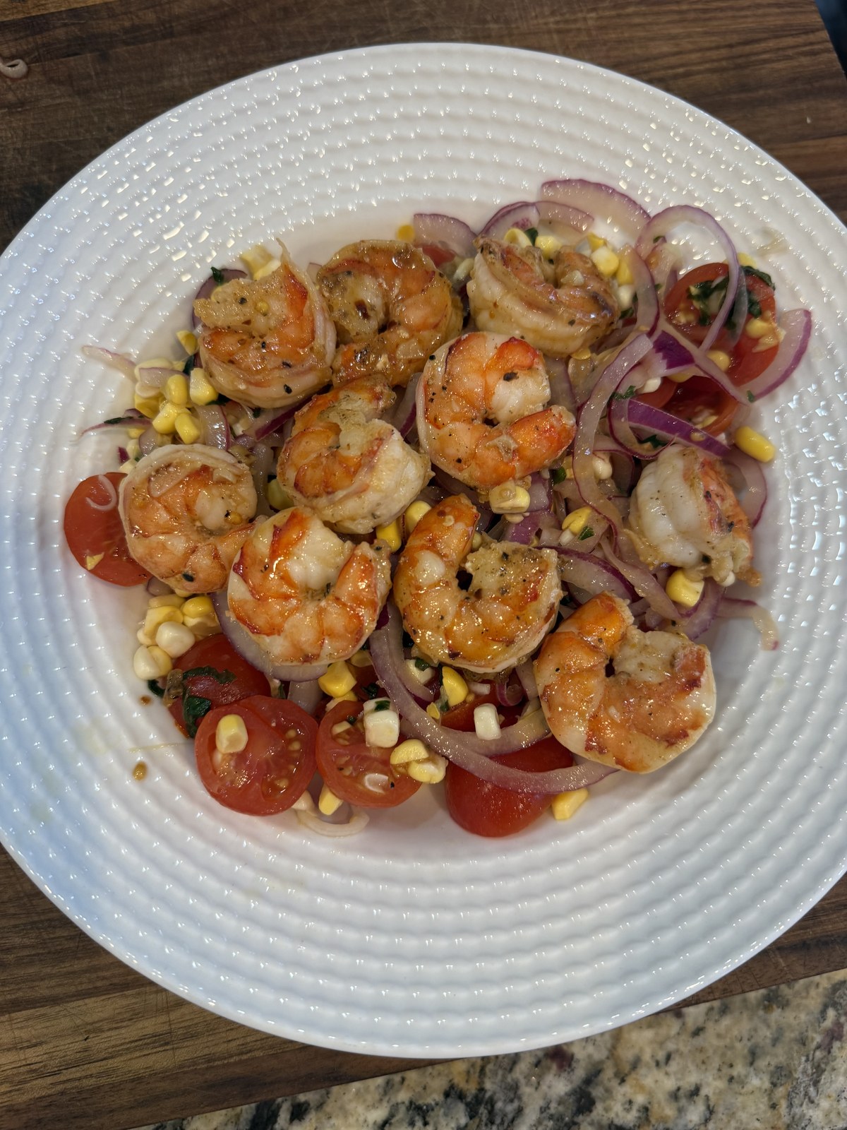 Seared garlic butter shrimp over a tomato, corn, and red onion salad on a white plate