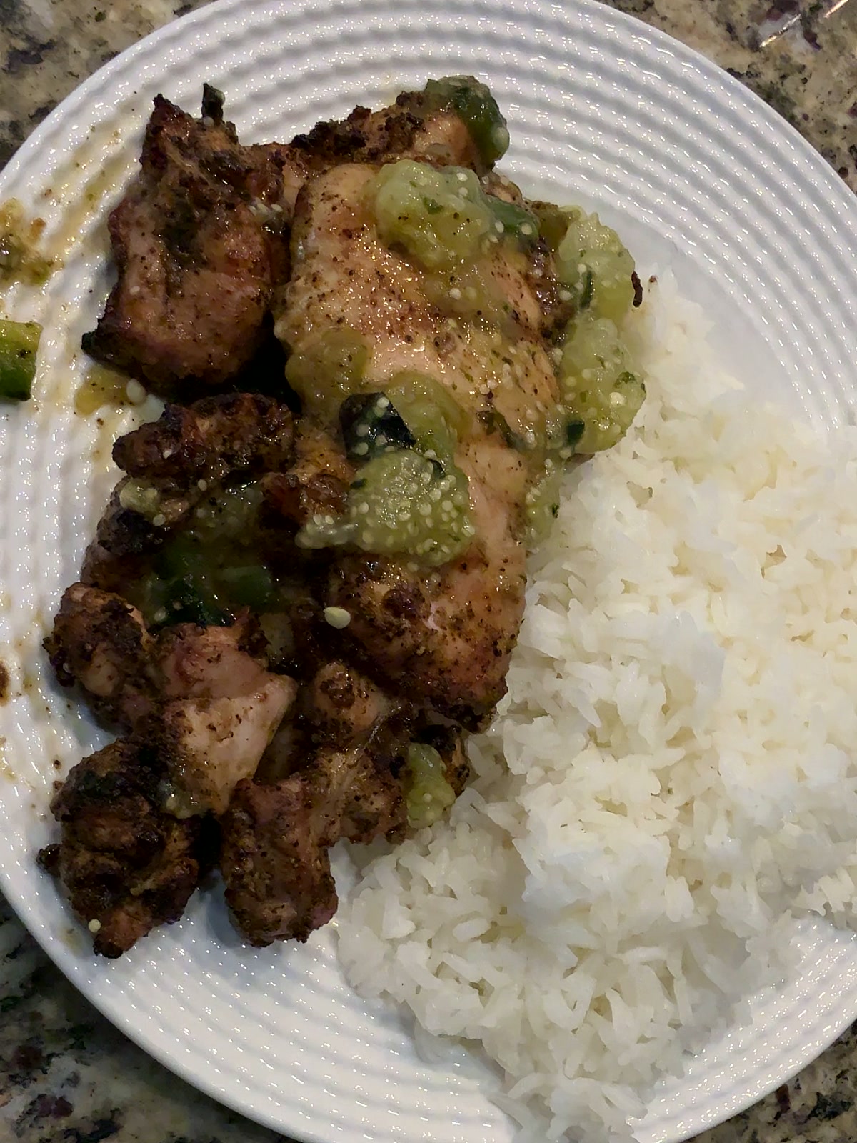 Grilled boneless chicken thighs on a white ribbed plate under a chunky green charred-tomatillo salsa, with white cilantro-lime rice alongside