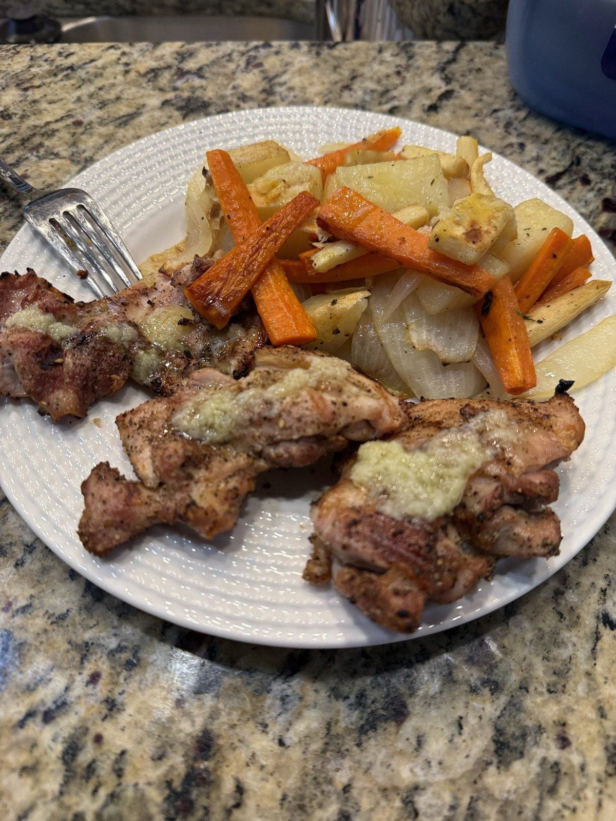 Grilled za'atar-crusted chicken thighs on a white plate beside roasted carrots, parsnips, potatoes, and onion