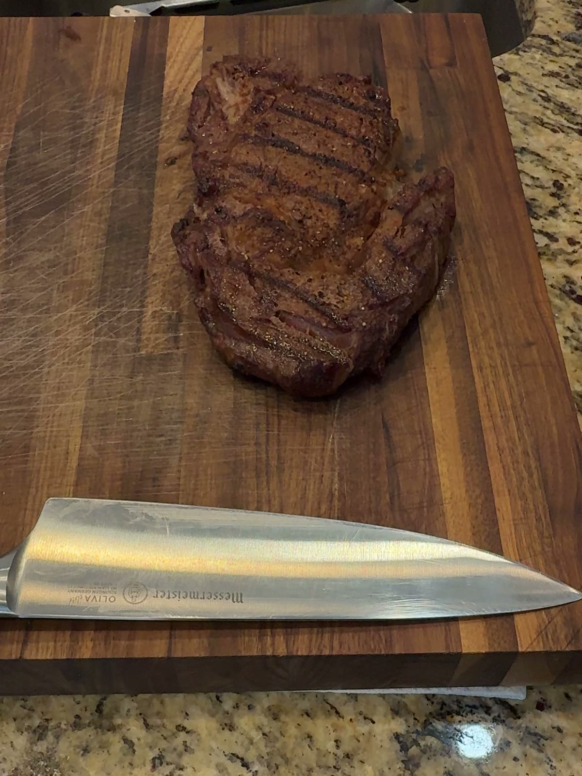 Grilled ribeye steak with a dark seared crust resting on a wooden board