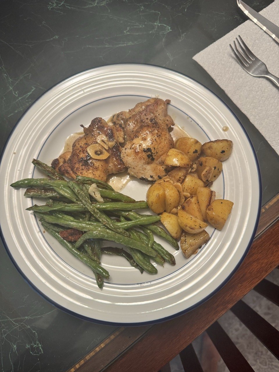 Crispy lemon chicken thighs with roasted lemon potatoes and blistered green beans on a white plate