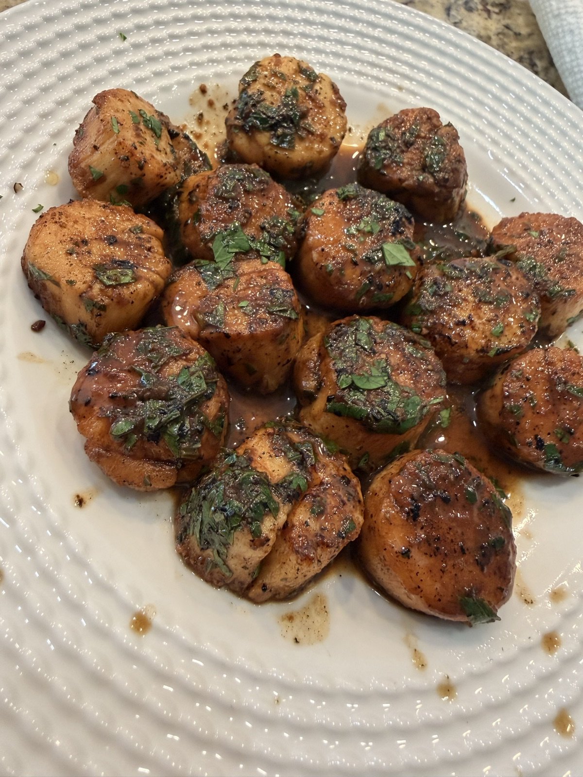 Seared scallops with golden crusts in a garlic-lemon pan sauce, scattered with chopped parsley, on a white plate