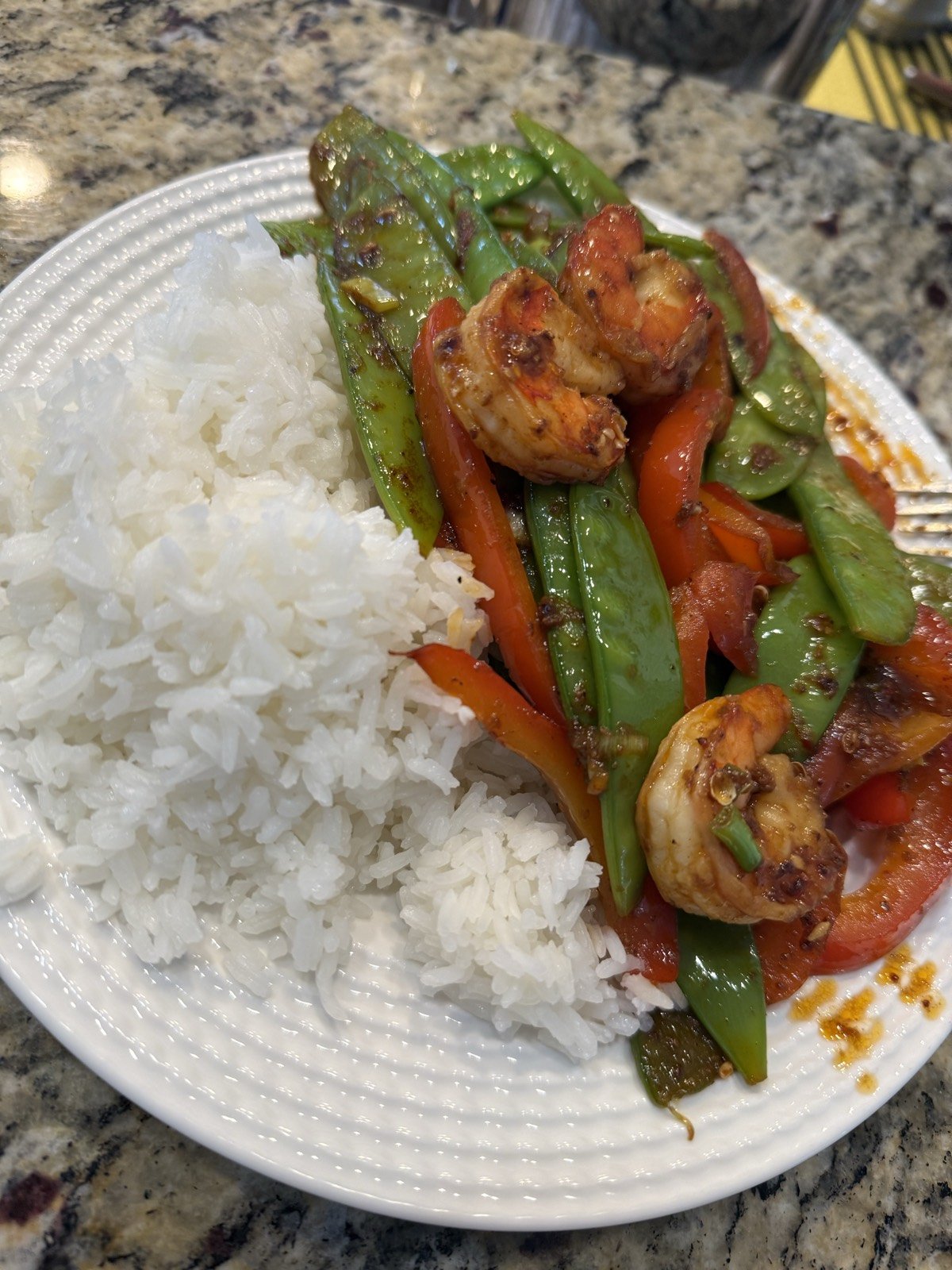 Seared shrimp with snow peas and red bell pepper over white rice on a white plate