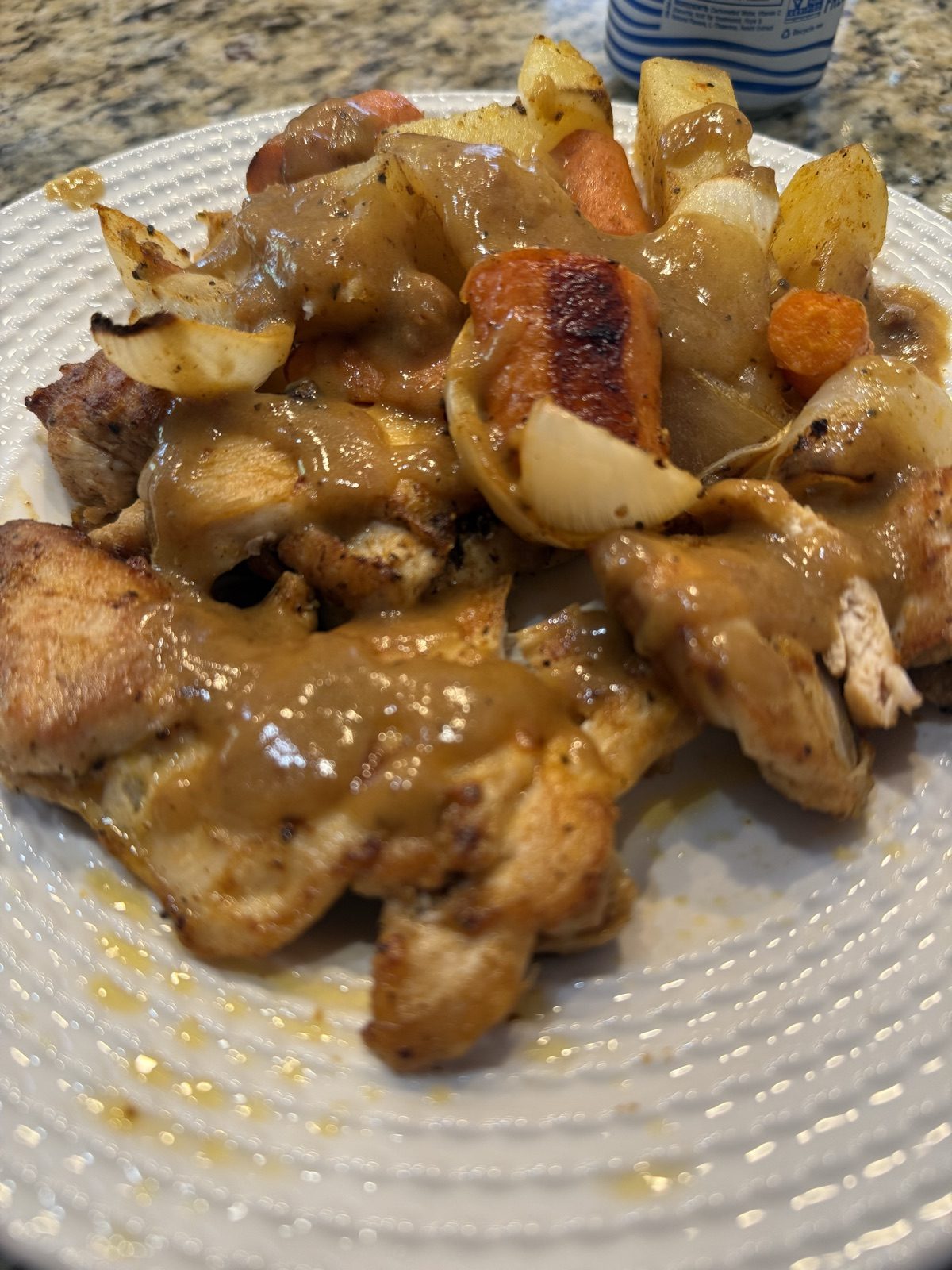 Sliced boneless chicken thighs under smoked paprika gravy with roasted carrots, potatoes, and onion on a white plate