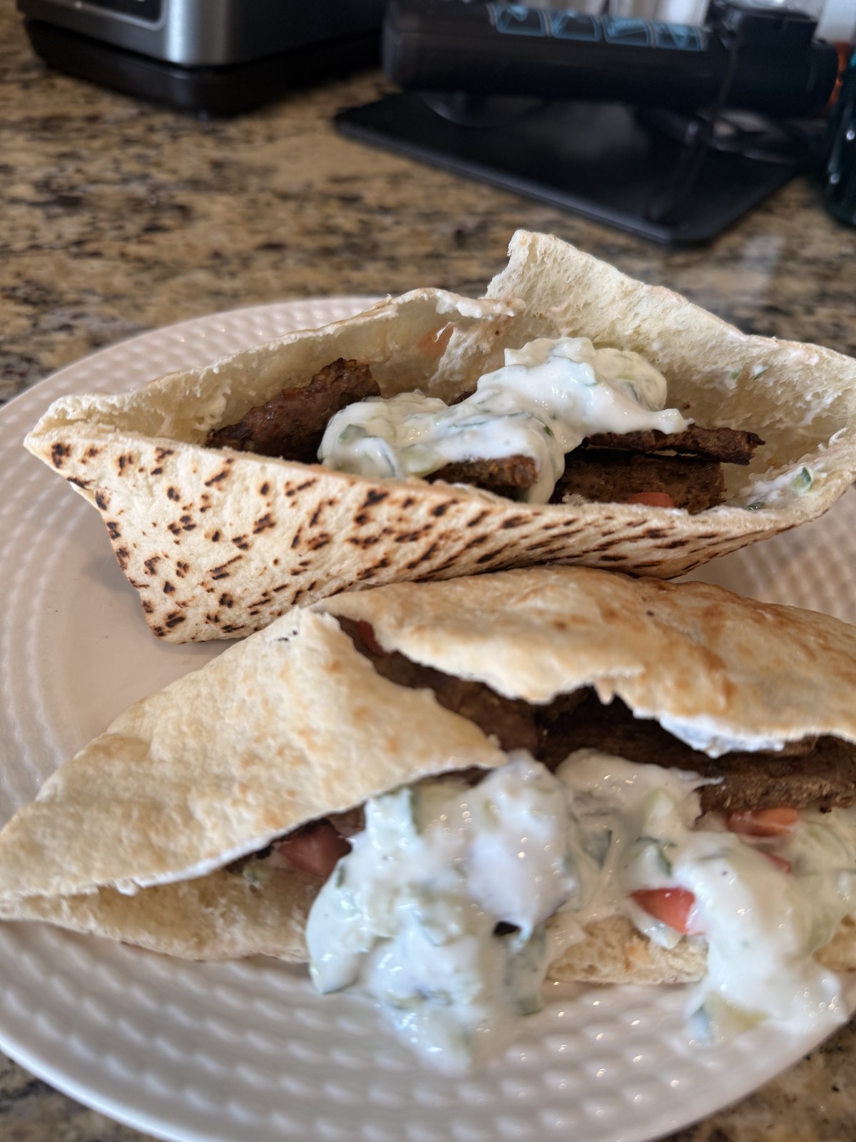 Two folded pita gyros on a white plate, filled with sliced spiced lamb, tzatziki, and tomato