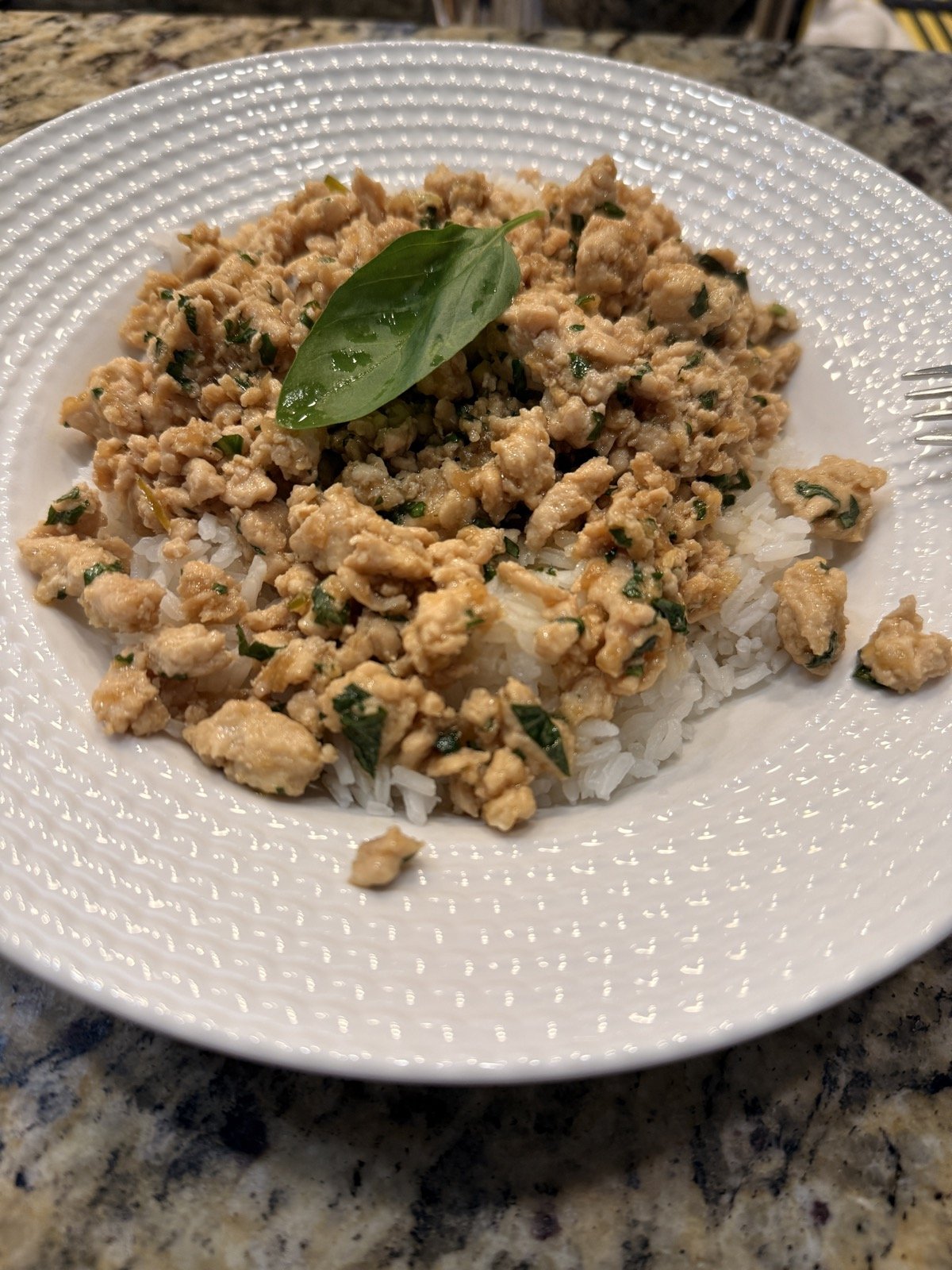 Ground chicken with basil served over white rice on a wide white plate